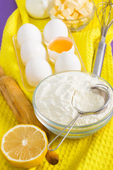 Fototapeta na wymiar Ingredients for baking lemon, a cup of flour, rolling pin, whisk and white eggs, yolk, butter on yellow background.