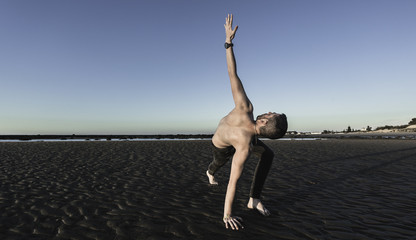 Hombre joven haciendo yoga en la arena de la playa
