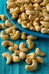 Heap of raw, organic, whole cashew nut kernels on blue plate