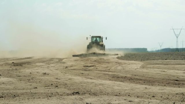 A tractor with an agricultural machine processes the soil, a lot of dust rises. The problem of soil erosion