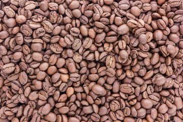 Coffee grains are scattered all over the surface. Fried coffee beans scattered by a heap.