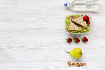 Healthy school lunch box with fresh fruits, organic vegetables sandwiches, fruits and bottle of water on white wooden background, flat lay. From above. Copy space.
