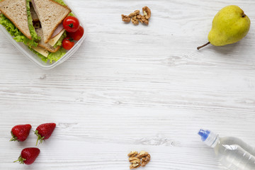 Healthy school lunch box with fresh organic vegetables sandwiches, walnuts, bottle of water and fruits on white wooden background, flat lay. From above. Top view. Space for text.