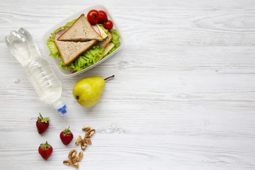 Healthy school lunch box with fresh organic vegetables sandwiches, walnuts, bottle of water and fruits on white wooden background, flat lay. From above. Top view. Copy space.