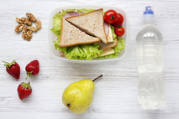 Lunch box with sandwiches, walnuts, bottle of water and fruits on white wooden table, top view. From above. Flat lay.