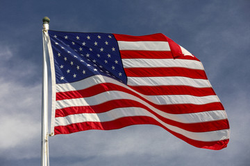 American flag waving in the wind with blue sky and white clouds in the background.