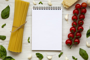 Ingredients for cooking pasta with notebook in the center on a white wooden background. Flat lay. From above. Top view. Copy space