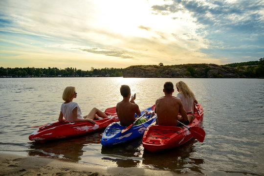 Friends Paddling Kayaks on the Beautiful River or Lake under Dramatic Evening Sky at Sunset