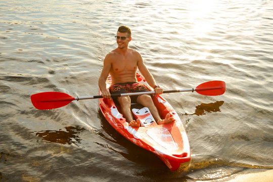 Young Happy Man Paddling Kayak on Beautiful River or Lake at Sunset