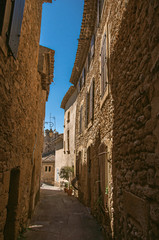 Fototapeta na wymiar View of typical stone houses with sunny blue sky, in a narrow alley of the historical village of Lourmarin. In the Vaucluse department, Provence-Alpes-Côte d'Azur region, southeastern France