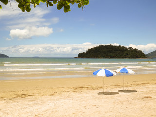 View of the sun day on the beach with sunshade, waves and island in the background.