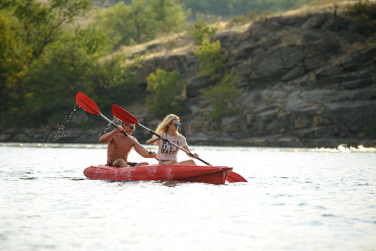 Young Couple Paddling Kayak on Beautiful River or Lake in the Evening