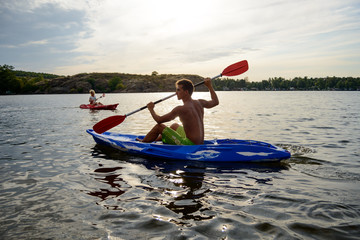 Young Man Paddling Kayak on the Beautiful River or Lake under Dramatic Evening Sky at Sunset