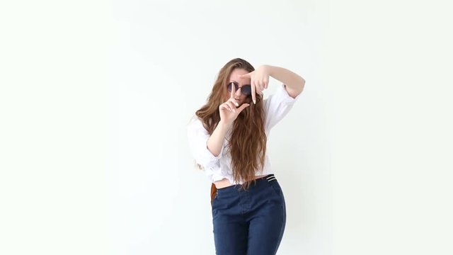 fashion of modern youth. stylish girl posing against white wall in jeans, white shirt, with leather backpack and glasses.