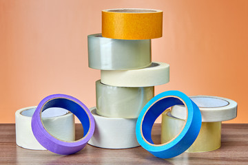 Different rolls of duct tape lie on table, orange background.