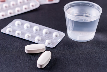 Water in plastic cup for taking of pills on black background
