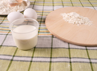 White eggs, milk and a plate of flour on a table.