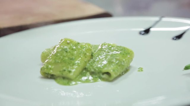 Close up, chef pours pesto and pappardelle on plate
