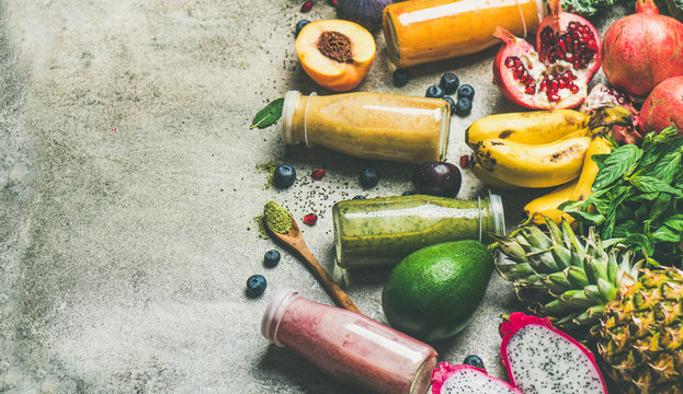 Colorful smoothies in bottles with fresh tropical fruit and superfoods on concrete background, copy space. Healthy, vegetarian, detox, dieting breakfast food concept