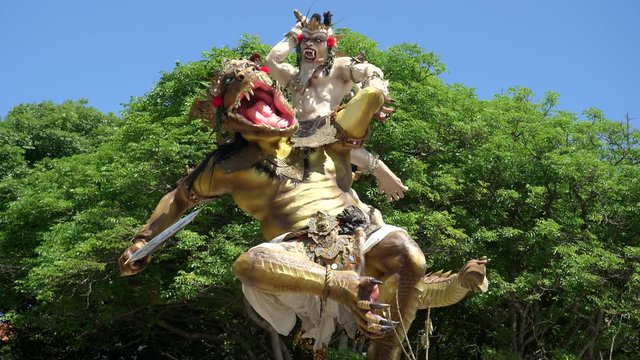 a hindu ogoh-ogoh statue in front of trees at kuta beach on the island of bali, indonesia
