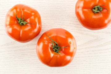 Three red tomato isolated on grey wood background top view.