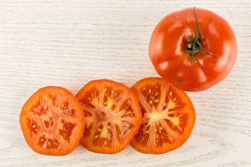One red tomato and three slices top view isolated on grey wood background.