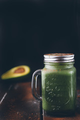 Green smoothie in jar with apple,avocado, and banana,on a wooden  board against a dark  background with chocolate powder.