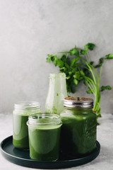 Green smoothie in jar with apple,baby spinach, parsley and banana, over a green round plate on a gray board against a gray background with parlsey leaves.
