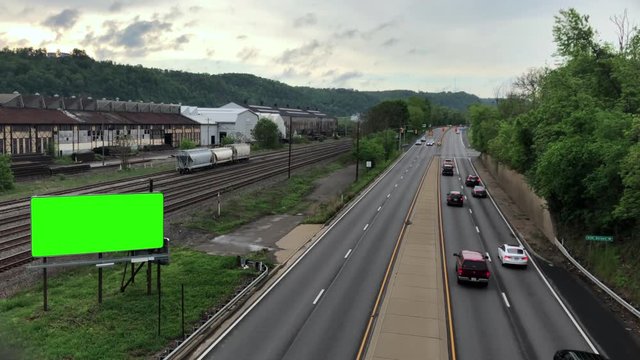 A high-angle overview of a highway and green screen billboard near old factories along the Ohio River at sunset. Pittsburgh suburbs.  	
