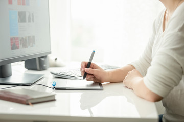 Fototapeta premium Closeup image of young female graphic designer holding stylus and working with graphic tablet