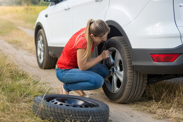 Young woman unscrewing car wheel nuts to change flat tyre