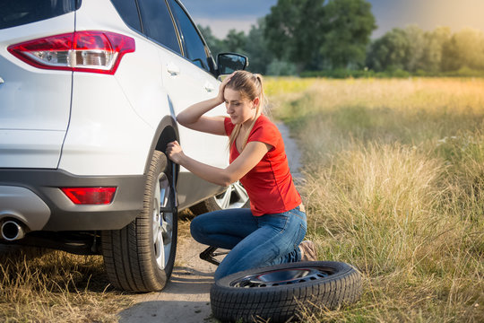 Upset Young Woman Looking On The Flat Tyre Of Her Car On Countryside Road