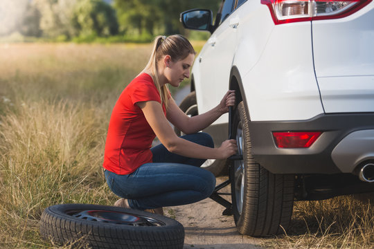 Toned image of young woman changing car flat tire with spare field in field