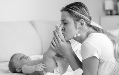 Black and white portrait of young mother kissing her baby son's feet