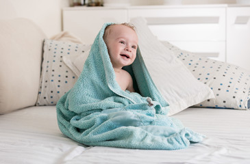 Portrait of cute smiling baby boy covered in big blue towel