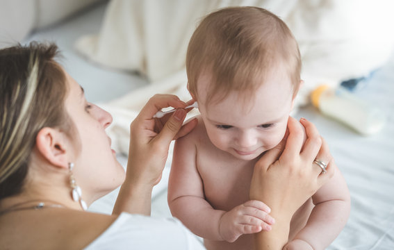 Young caring mother clearing baby son's ears from earwax with cotton swab