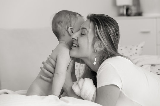 Black and white portrait of young caring mother hugging her baby son sitting on bed