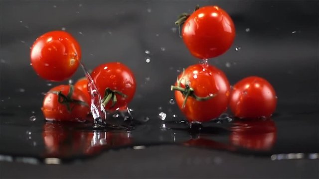 Super Slow Motion of Red Fresh Tomatos Falling with Water Splash on Black Surface