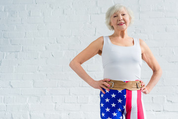 happy senior woman in sportswear standing with hands on waist and smiling at camera