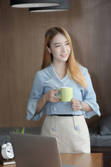 businesswoman in casual wear smiling and holding green cup while standing in office