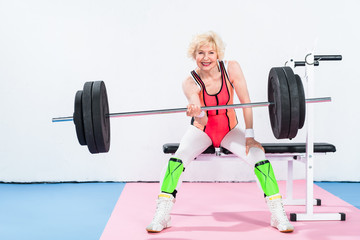 Fototapeta na wymiar happy senior sportswoman lifting barbell and smiling at camera