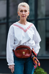 fashionable senior woman in trendy outfit posing with belt bag