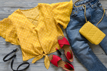 Womens clothing, accessories, shoes (yellow blouse in polka dot, blue jeans, leather red sandals,  yellow crossbody bag, lipstick). Fashion outfit. Shopping concept. Flat lay. Trendy, saturated colors