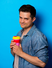 Young man in jeans shirt with colorful cup on blue background