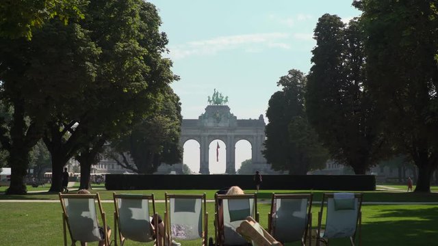 Triumphal Arch view from a  Cinquantenaire Park, where people walk and with deck chairs in the front on a sunny day..Brussels, Belgium
