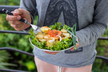 Woman hands holds backed, stewed new potato with onion rings, homemade tomatoes ketchup sauce on green salad leaves and onion. Raw vegan vegetarian healthy food