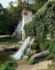 a waterfall near a wall with greenery near an old dilapidated mansion