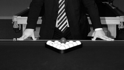 a man in a suit leans his hands on a pool table, on which there are billiard balls