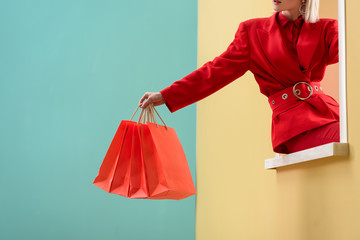 cropped shot of fashionable woman in red clothing with red shopping bags sitting on decorative...