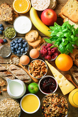 Healthy breakfast ingredients, food frame. Granola, egg, nuts, fruits, berries, toast, milk, yogurt, orange juice, cheese, banana, apple on wooden rustic background, top view, copy space.